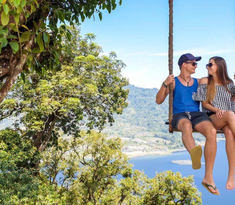 A couple enjoying their time on the swing with The Twin Lake behind them, Bali, Indonesia. The swing is attached to a tree very high above the lake. Couple is having a lot of fun. Touristic attraction